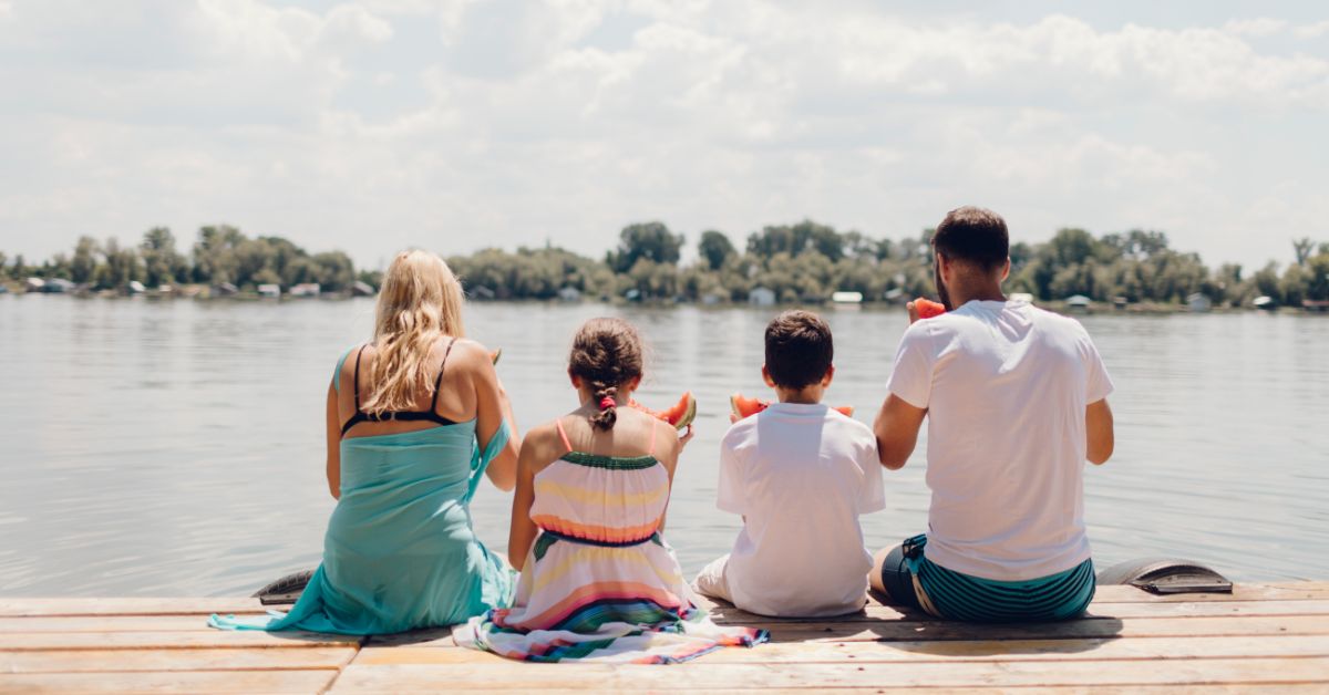Family of four sitting on a lake dock with feet hanging over the dock looking out over the water