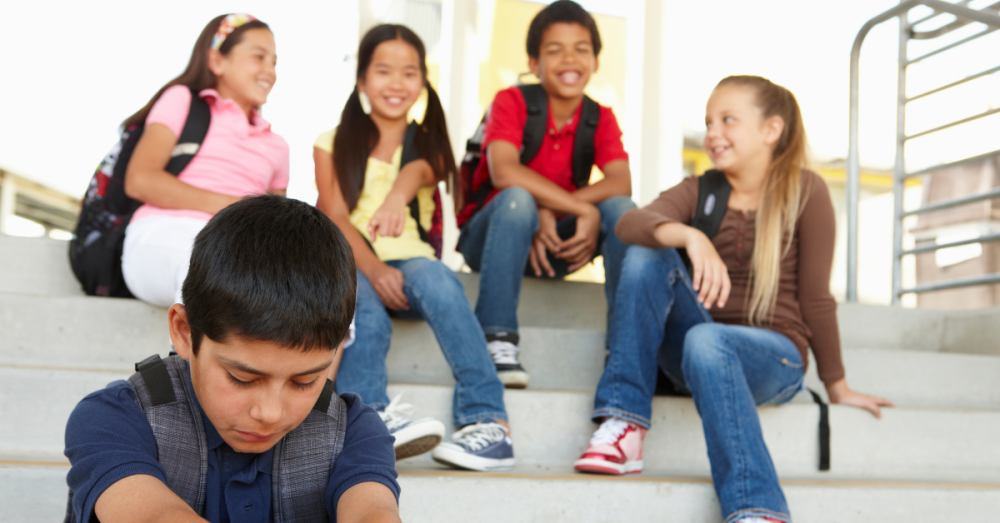 A group of children surrounds another child, teasing and pointing, while the bullied child looks down in distress.