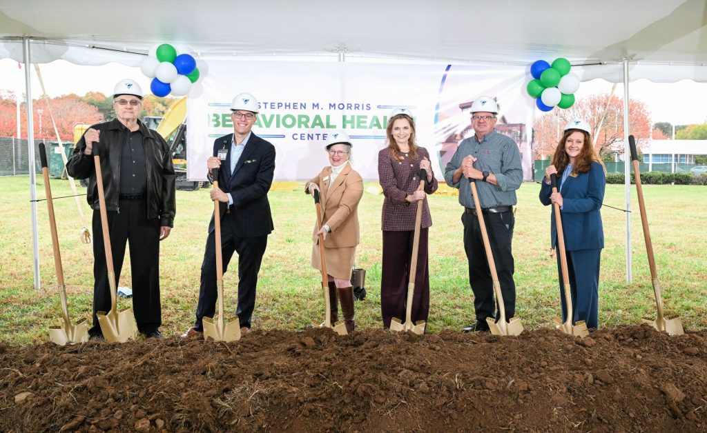 a group of Monarch leadership holding shovels in front of a white tent for a groundbreaking event