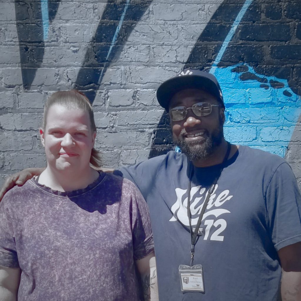 Two friends posing against mural.