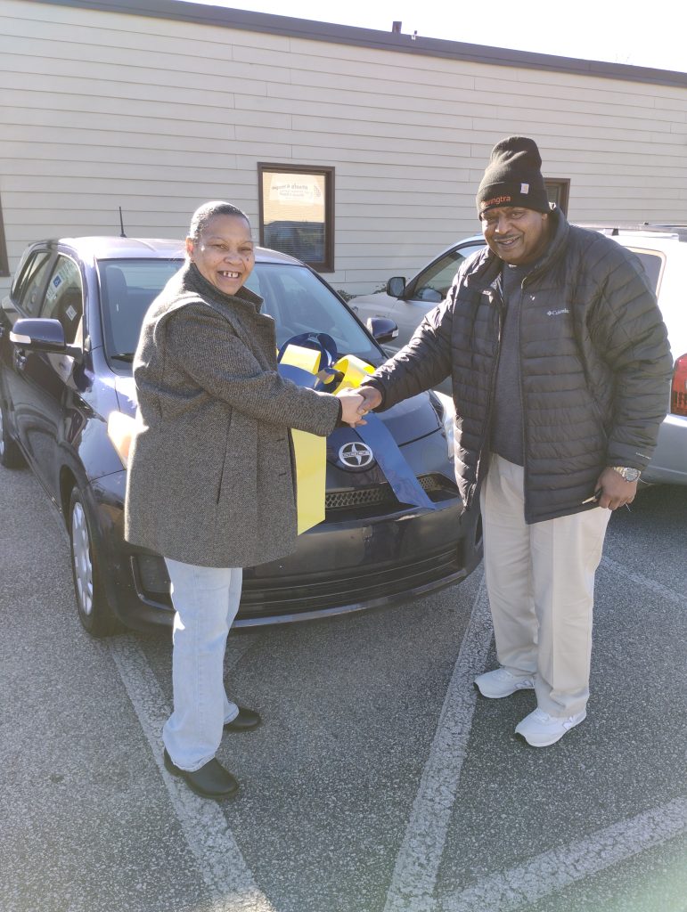 Man (Stacey Price) shaking hands with woman (His Tailored Care Management Care Manager, Rosa Pulley Bryant) by a car.