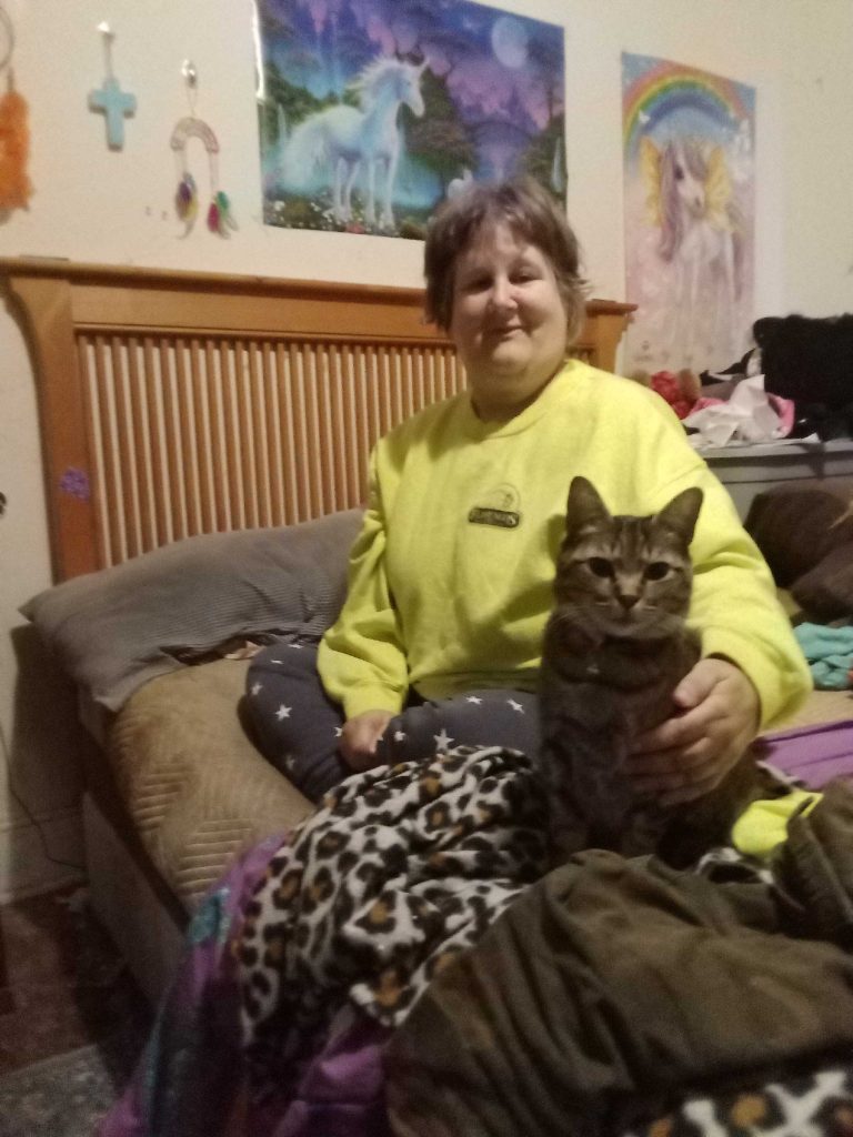 Kristine Maher sitting with a brown cat on her bed and smiling.