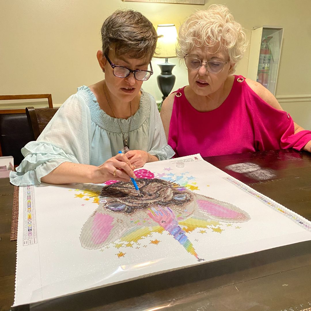 a resident at Monarch’s Lafayette Group Home in Albemarle, works on a diamond art project with her mom, Penny, admiring her work.