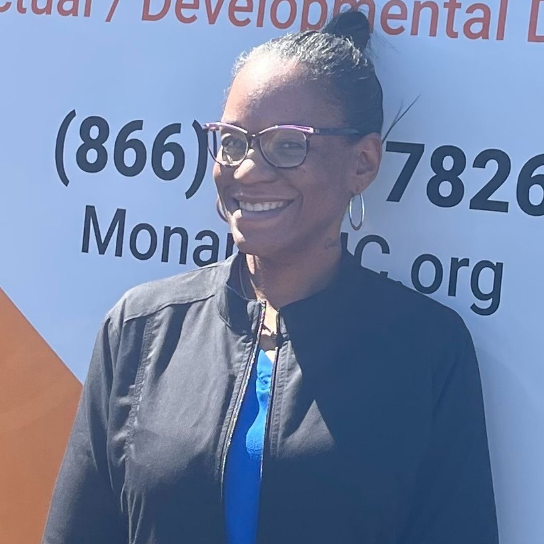 Registered Nurse Nicole B. Richardson in front of Monarch's Mobile Integrated Care Clinic dressed in a black jacket, wearing glasses and smiling.