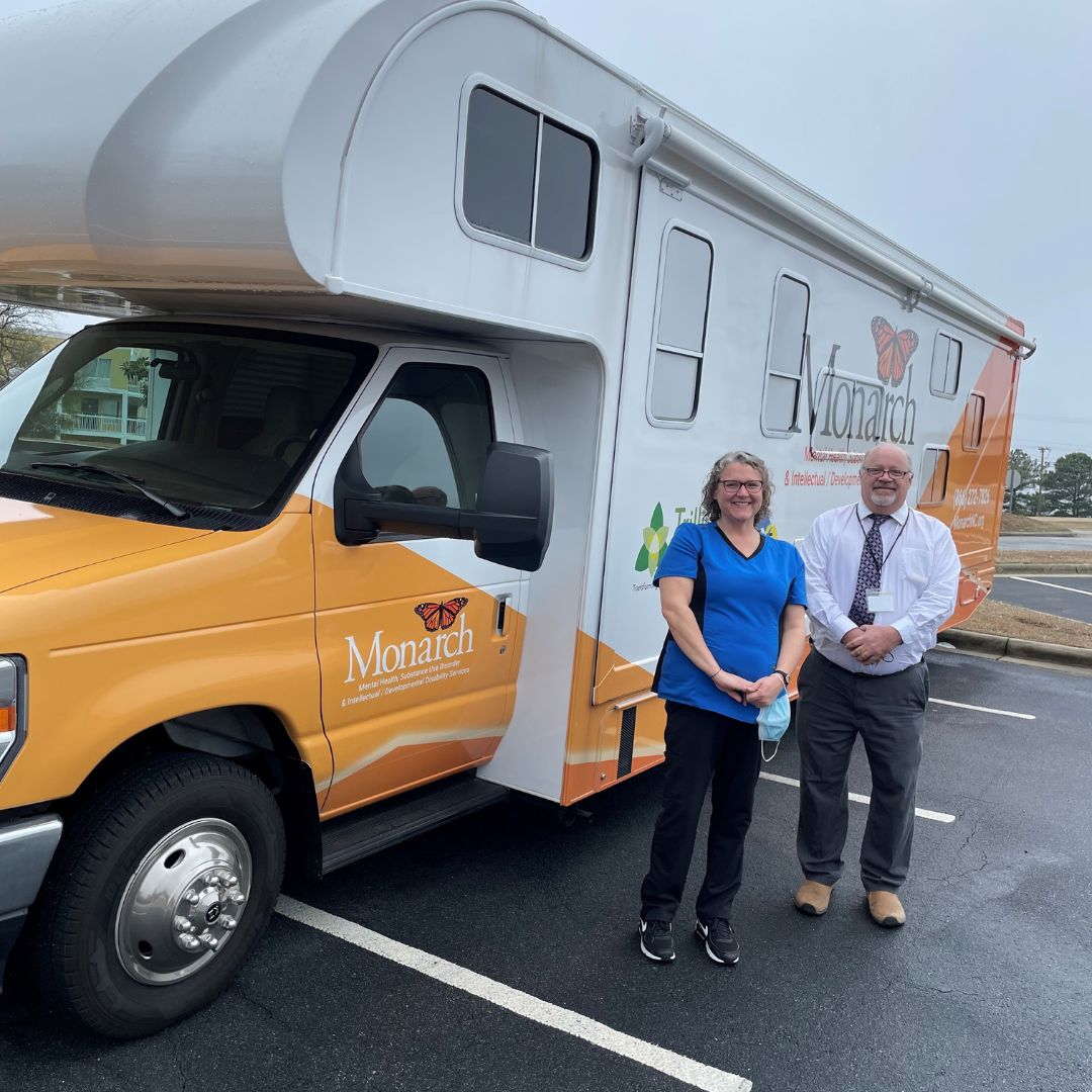 : Mobile Integrated Care Clinic Team Lead Kelly Hagwood, RN, and Peer Support Specialist Winston Thomas pose in front of Monarch’s second clinic developed in partnership with Trillium Health Resources.