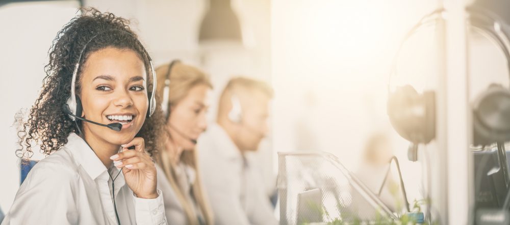 Call center employee near fellow staff, smiling and wearing headset.