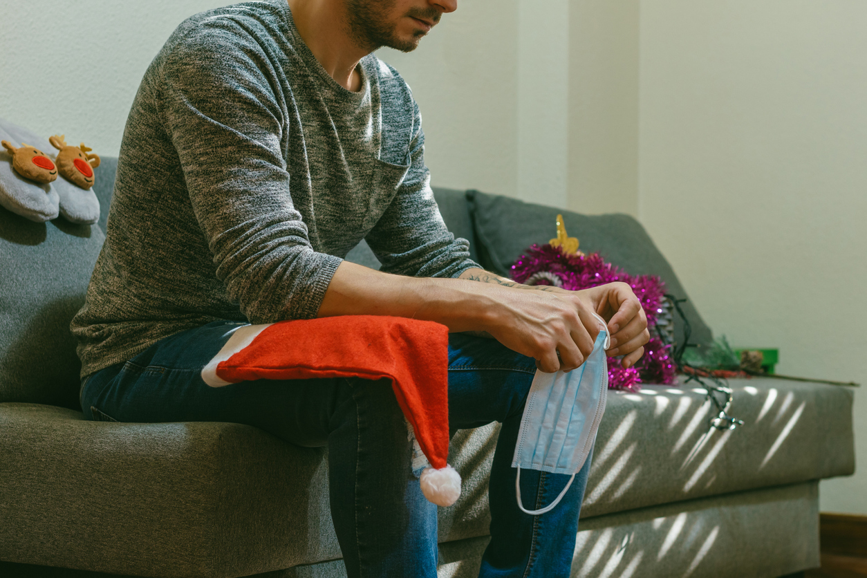 Man holding a facemask sitting on a couch preparing for the holidays.