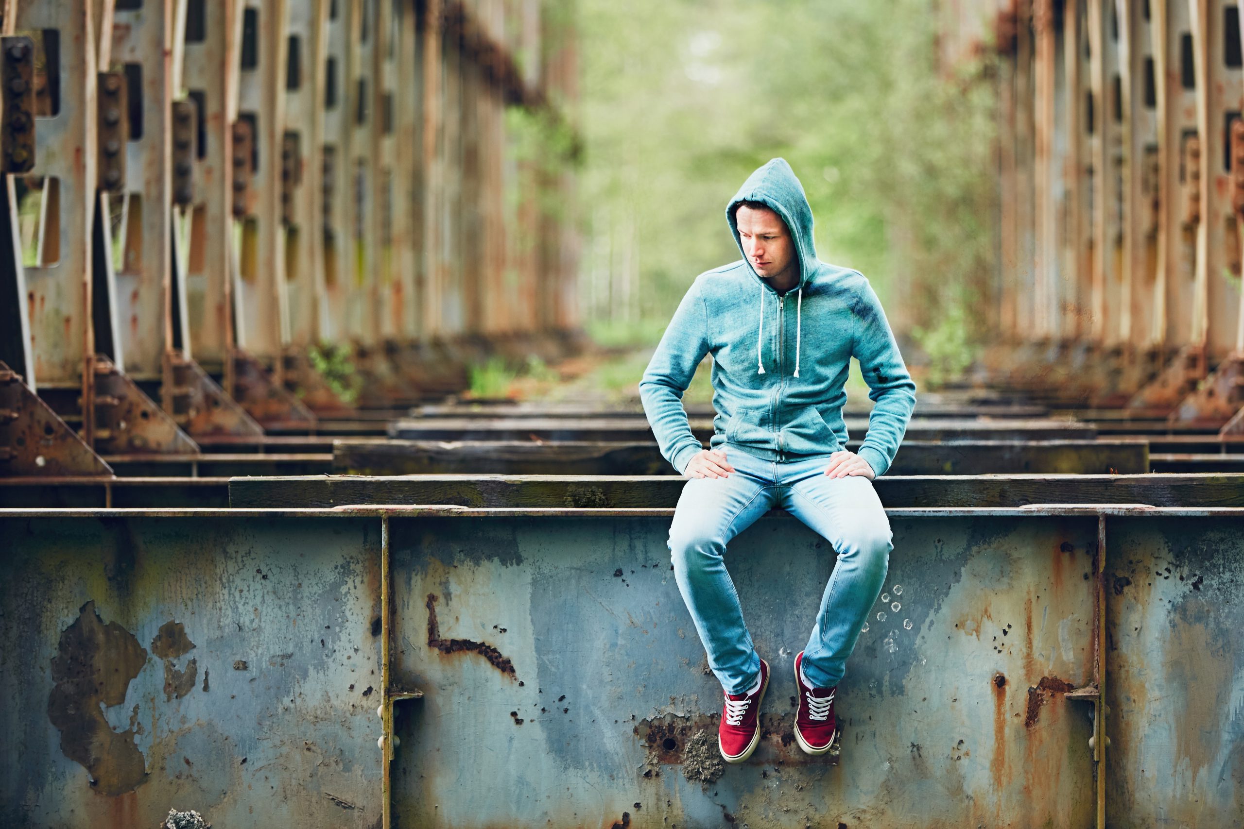 Man in hoody sitting, pondering, on bridge